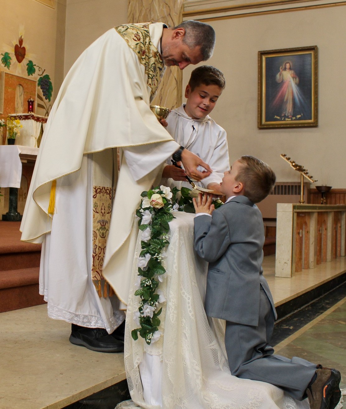 Fr. Silvio giving First Communion to a students kneeling looking up